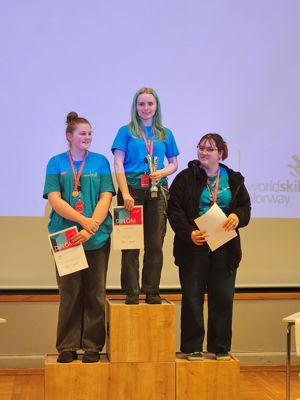 Tre jenter på et podium med diplom og medalje