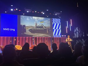 Publikum ser på presentatør på scenen med skjerm i bakgrunnen med stridsvogn fra Ukraina.